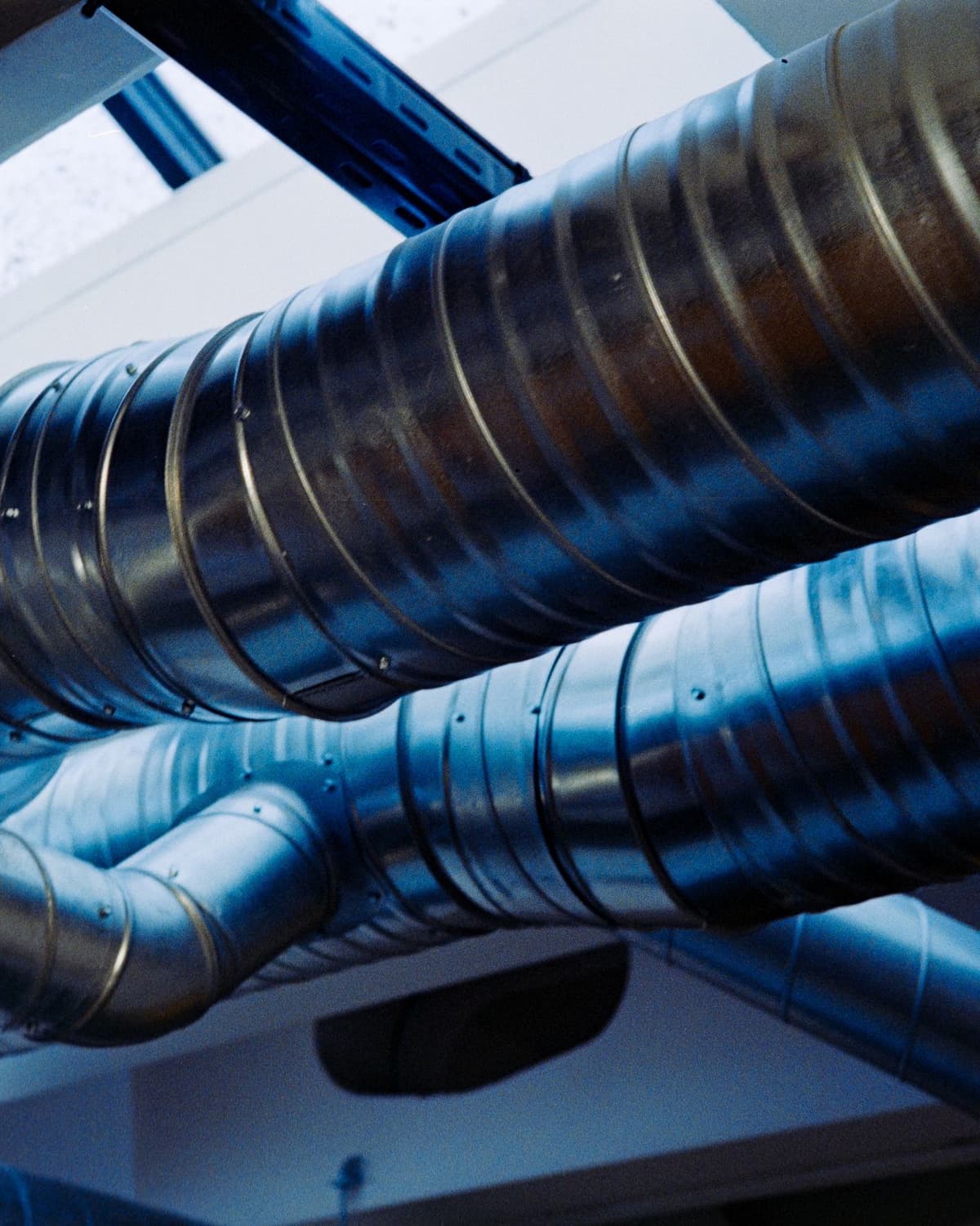 Large spiral metal ductwork running along a ceiling in a bright building